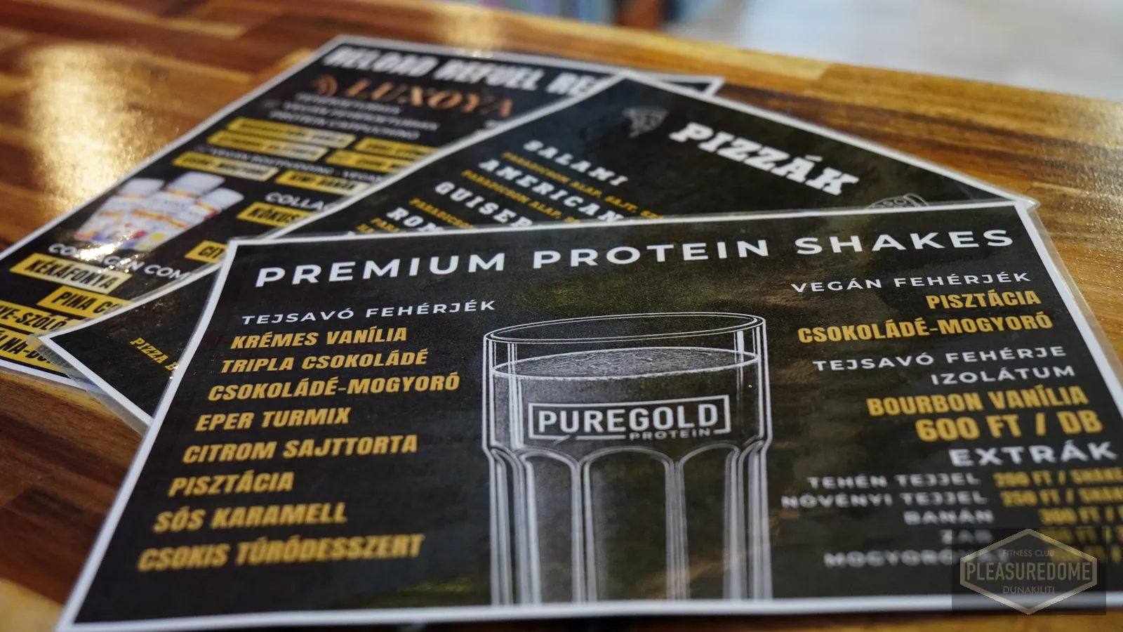 Pleasuredome protein shake, pizza és táplálékkiegészítő étlap a kávézó pultján — Puregold protein, Luxoya kollagén és vegán fehérjék