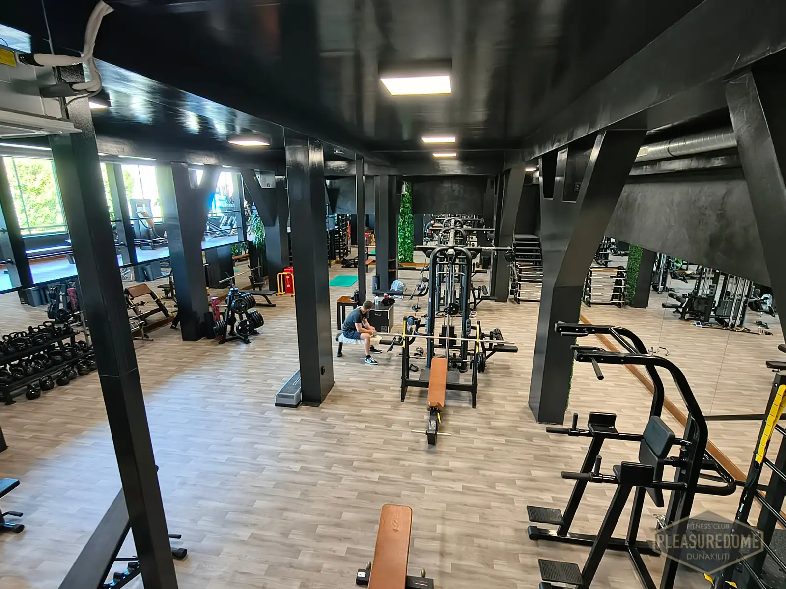 Erősítő zóna fekete oszlopokkal, szabad súlyokkal és gépekkel a Pleasuredome Fitness Clubban